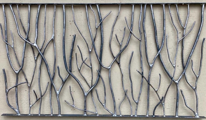 May include: Metal wall art featuring a stylized forest scene. The artwork is composed of numerous silver-colored metal branches and twigs, creating a textured, naturalistic design. The branches are welded together, forming a rectangular shape.