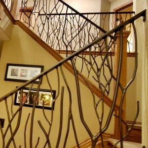 May include: A staircase with a custom metal railing featuring a tree branch design. The railing is dark brown and complements the wooden handrail and steps. Two framed photos hang on the beige wall. The overall design creates a natural, artistic aesthetic.