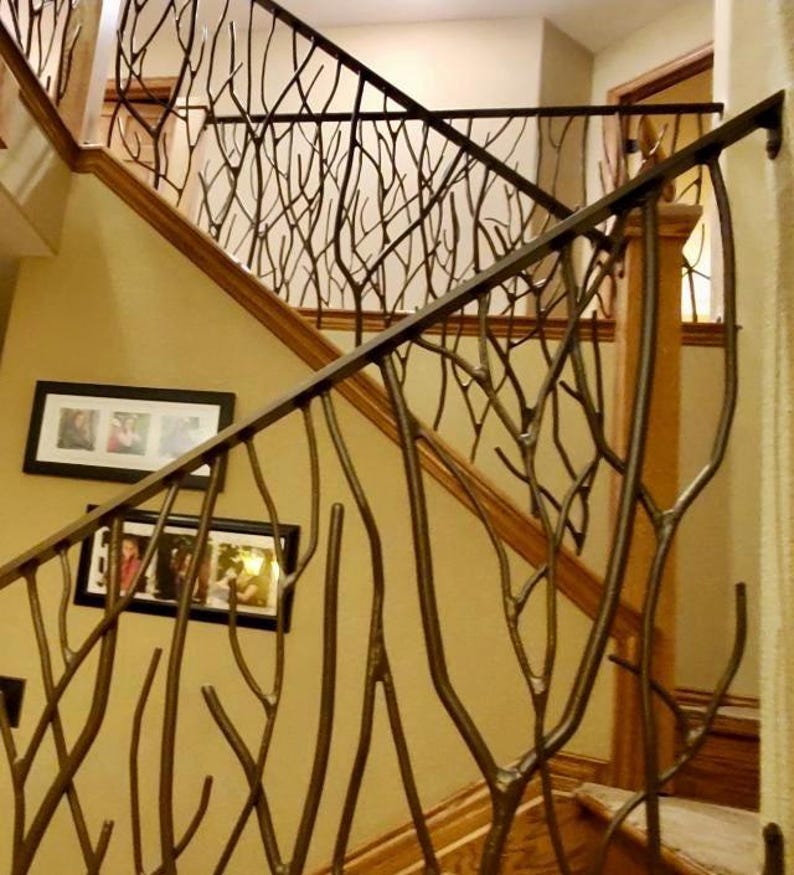 May include: A staircase with a custom metal railing featuring a tree branch design. The railing is dark brown and complements the wooden handrail and steps. Two framed photos hang on the beige wall. The overall design creates a natural, artistic aesthetic.