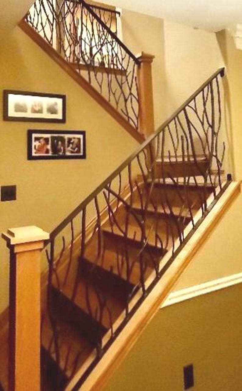 May include: A wooden staircase with a decorative wrought iron railing. The railing has a branch-like design. The stairs are made of wood and lead upwards. The walls are painted a warm beige color. Two framed pictures hang on the wall.