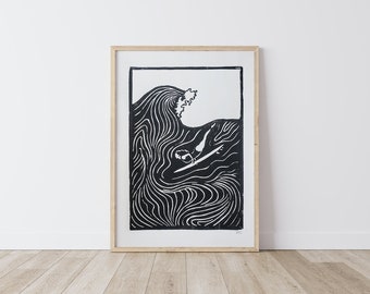 May include: Black and white linocut print of a surfer riding a wave. The print is framed in a natural wood frame.