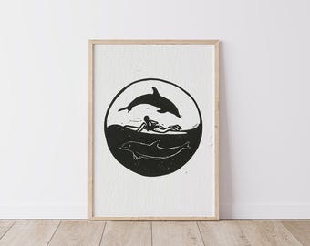 May include: Black and white illustration of a surfer riding a wave with a dolphin jumping above them. The image is framed in a simple wooden frame.