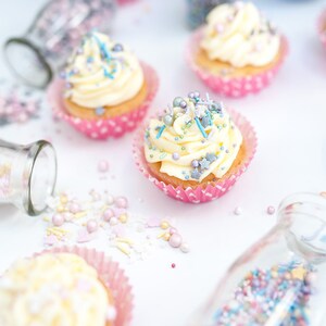 4 cupcakes decorated with buttercream and edible sprinkles. Also sprinkles in a glass jar.