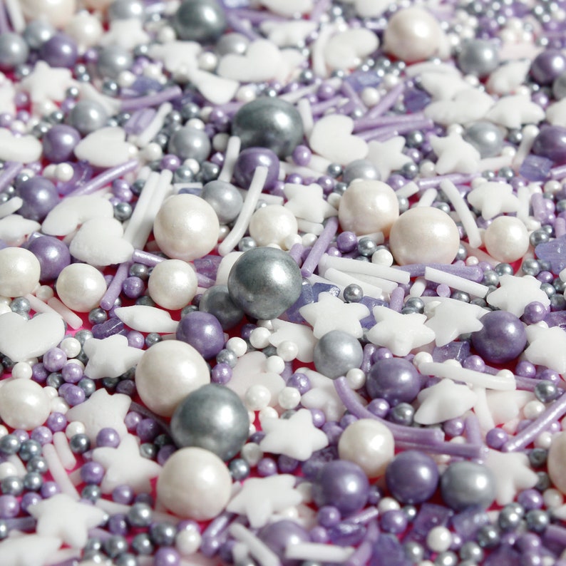 Purple, silver and white cake sprinkles featuring edible stars, hearts, sugar strands, nonpareils, sugar rocks and pearls.