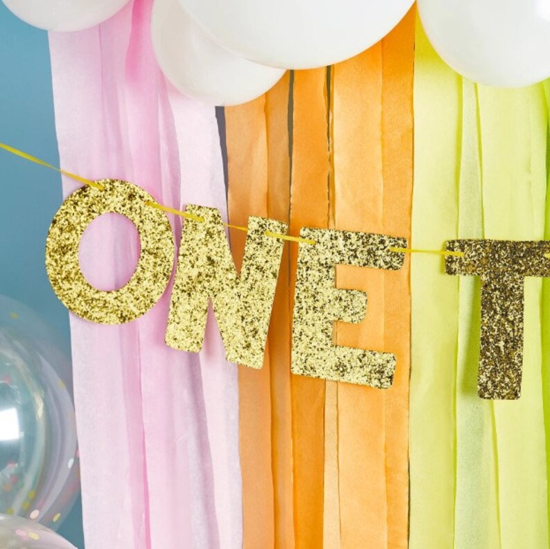 Pink, yellow and orange tissue paper background with gold glittery one today garland.