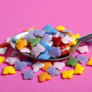 Yellow, white, red, green, blue, purple and yellow butterfly shaped cake sprinkles on a teaspoon.