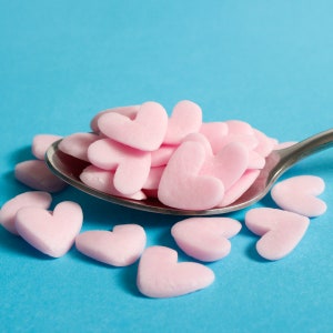 Pink jumbo heart shaped edible cake sprinkles on a spoon.