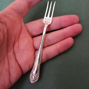 May include: A silver fork with an ornate handle and the words "Spit the Bit" engraved on the handle.