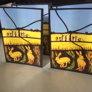 Tarjetas de felicitación de liebres de primavera en Stonehenge, piedras en pie de Clare Maryan Green, artista de vidrieras.