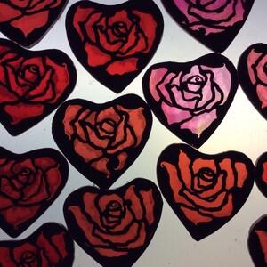 A group of  heart-shaped ornaments with black outlines and red and pink roses painted inside. The ornaments are perfect for Valentine's Day or any occasion.