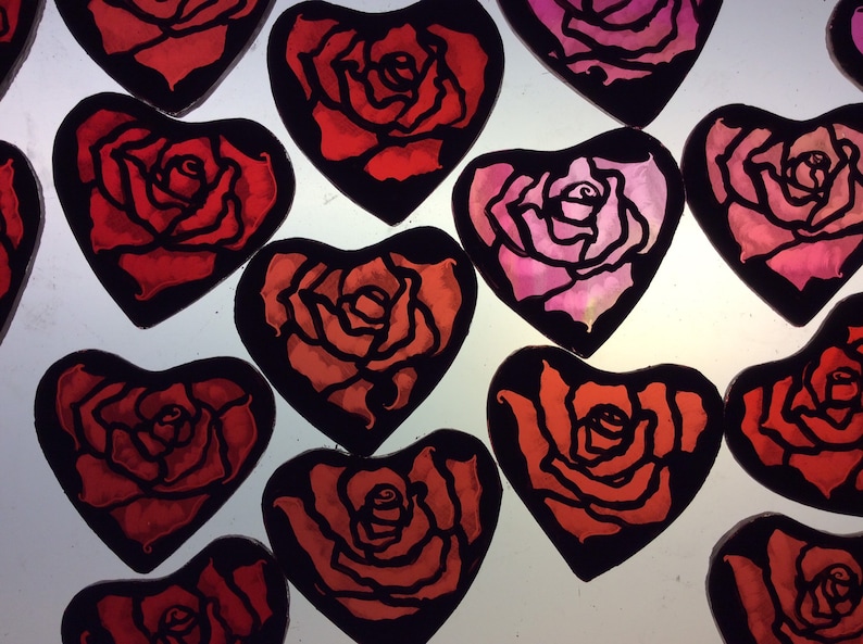 A group of  heart-shaped ornaments with black outlines and red and pink roses painted inside. The ornaments are perfect for Valentine's Day or any occasion.