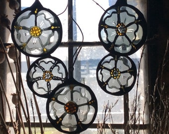 May include: Five white glass ornaments with black outlines and gold accents, shaped like roses, hanging in front of a window.