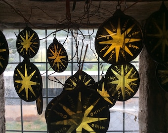 May include: A collection of round, black glass ornaments with gold star designs hanging from a window. The ornaments are suspended by thin wires.