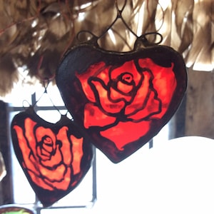 Two red stained glass hearts with black outlines, each featuring a hand painted rose design. The hearts are hanging from a hand madewire loop.