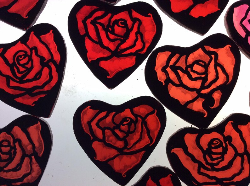Eight red heart-shaped stained glass ornaments with black outlines, each featuring a stylised red rose design.  The roses are shown on a light box where they have been painted.  The red colour varies a little from one decor to the next.