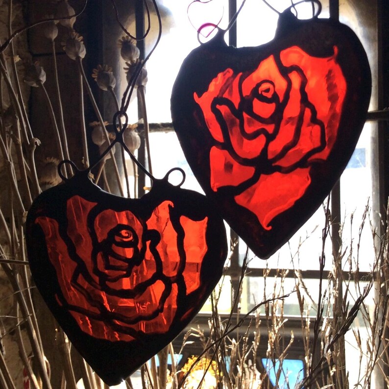 Two beautiful red rose stained glass hearts, hanging in a window.  The suncatchers have decorative copper hooks to hang from.