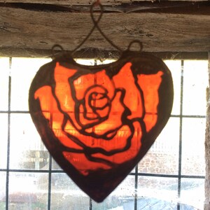 A stained glass heart-shaped window hanging with a red rose design.
