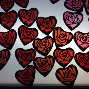 Work in progress picture of 17 heart-shaped ornaments featuring rose designs. The ornaments are painted in shades of red and pink.