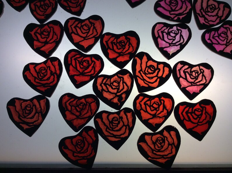 Work in progress picture of 17 heart-shaped ornaments featuring rose designs. The ornaments are painted in shades of red and pink.