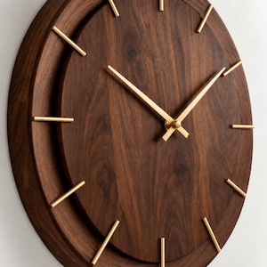 May include: A circular wall clock featuring a dark brown wood grain face and a matching wooden frame. The clock has thin, metallic gold-colored hour markers and matching gold-colored hour and minute hands centered on the dial.