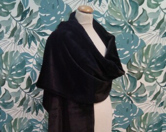 May include: A black faux fur shawl draped over a mannequin against a backdrop of green and blue tropical leaves.
