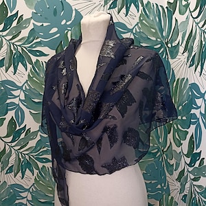 May include: A navy blue sheer scarf with a silver leaf pattern. The scarf is draped over a white mannequin.