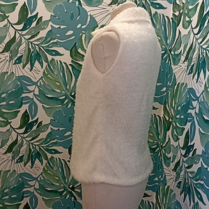 May include: White fluffy sleeveless vest with a high neck.