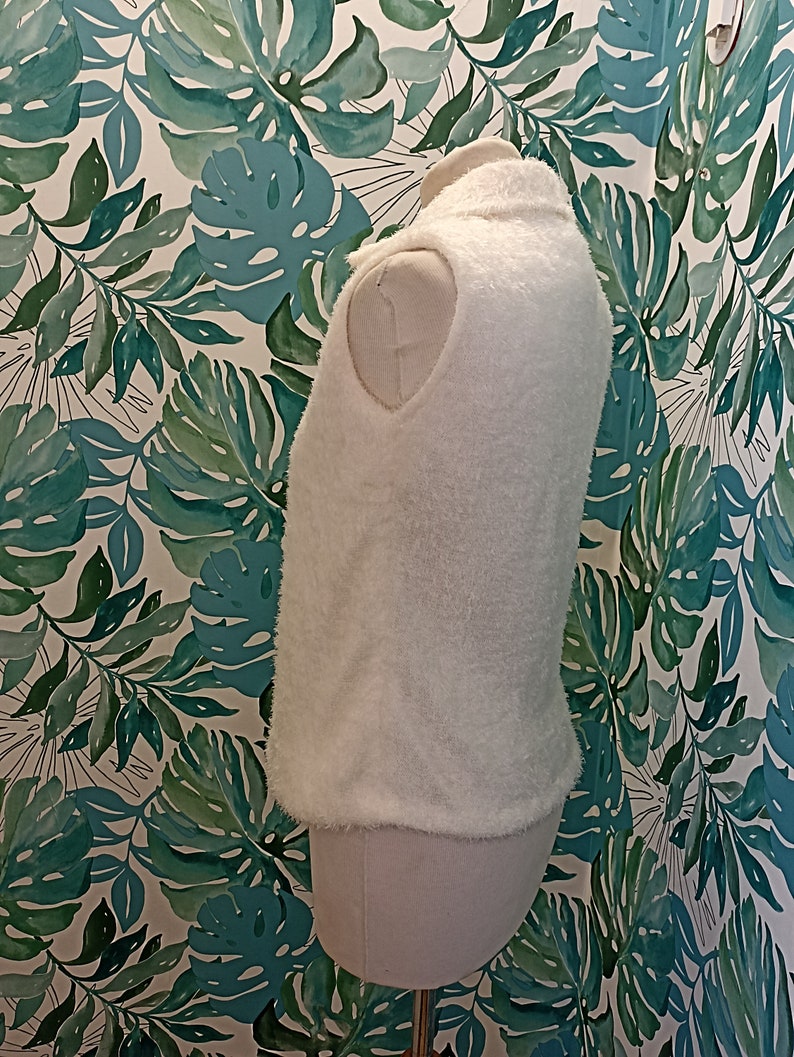 May include: White fluffy sleeveless vest with a high neck.