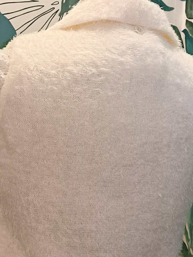 May include: A white fluffy sweater with a collar and a button fastening.