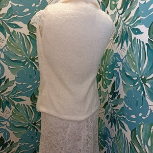 May include: A white fluffy sleeveless sweater with a lace skirt. The sweater has a collar and the skirt is A-line.