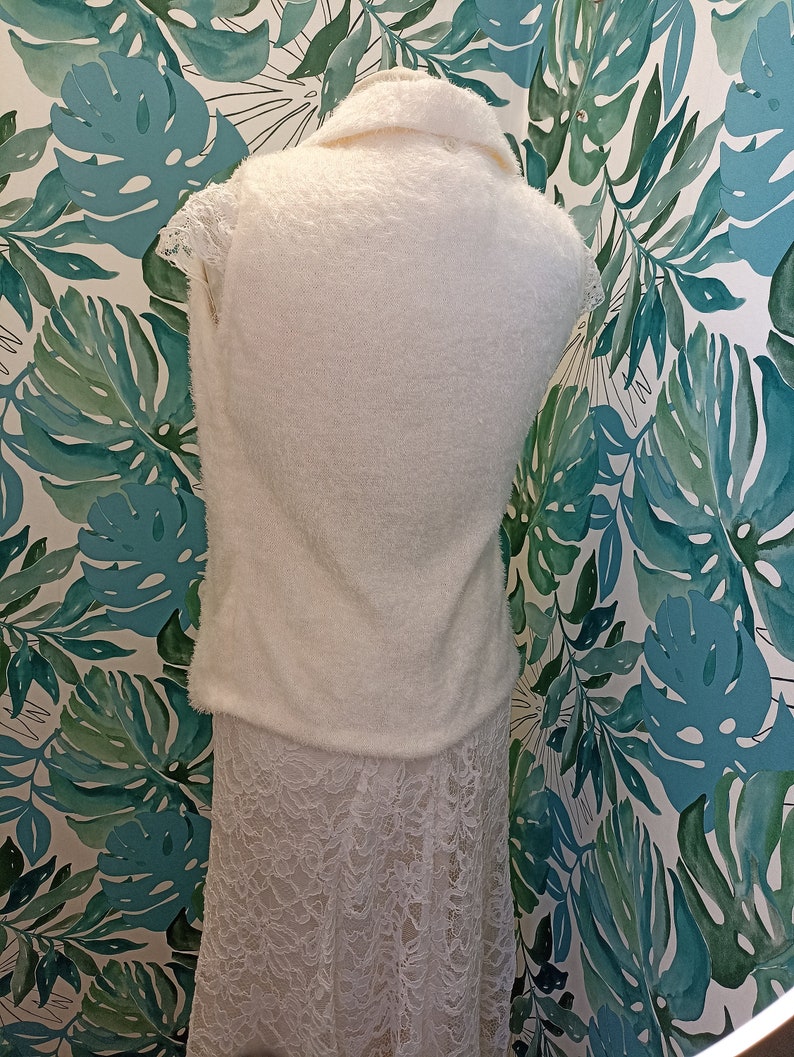 May include: A white fluffy sleeveless sweater with a lace skirt. The sweater has a collar and the skirt is A-line.