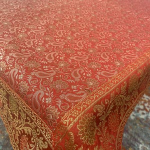 Puede incluir: Mantel de mesa rojo con estampado de paisley dorado y borde dorado.