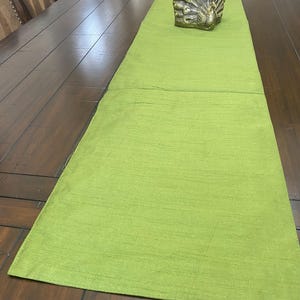 May include: A green table runner with a subtle texture. The runner is laid out on a wooden table with a gold peacock figurine on top.