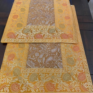 May include: Two gold table runners with intricate floral patterns and a brown center. The runners have a gold border with a white trim.