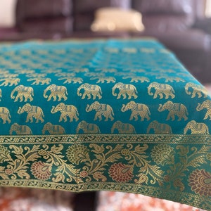 May include: A teal tablecloth with a gold elephant pattern and a gold and green floral border.