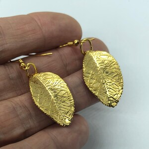 Puede incluir: Un par de pendientes colgantes de hoja de oro con una superficie texturizada.