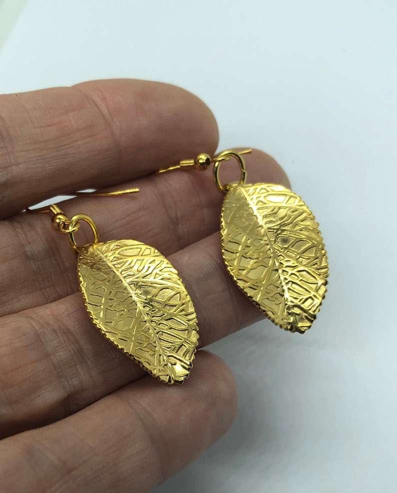 Puede incluir: Un par de pendientes colgantes de hoja de oro con una superficie texturizada.