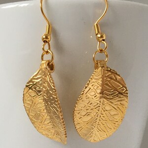 Puede incluir: Un par de pendientes colgantes de hoja de oro con un dise&ntilde;o delicado e intrincado. Los pendientes tienen un cierre de gancho.