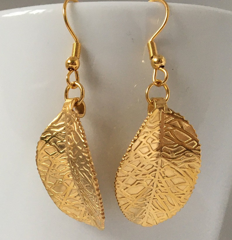 Puede incluir: Un par de pendientes colgantes de hoja de oro con un dise&ntilde;o delicado e intrincado. Los pendientes tienen un cierre de gancho.