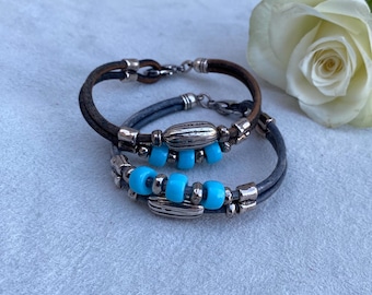 May include: Two leather bracelets with silver accents and turquoise beads. The bracelets are layered on top of each other.