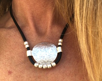 May include: A silver hammered metal pendant necklace with a black leather cord and silver beads.