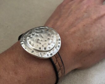 May include: A silver hammered metal bracelet with a brown leather strap.