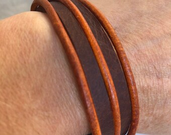 May include: A brown leather bracelet with three layers of leather. The bracelet is worn on a person's wrist.
