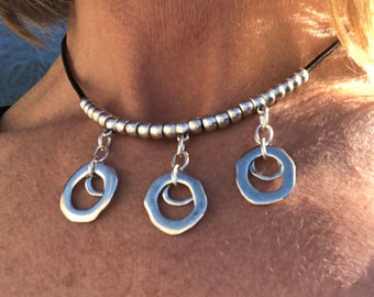 May include: A silver choker necklace with three dangling silver circles. The circles are slightly irregular in shape and have a hammered texture.