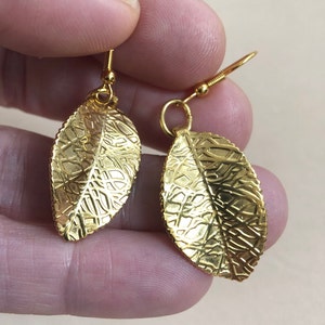 Puede incluir: Un par de pendientes de hoja de oro con una superficie texturizada. Los pendientes tienen un dise&ntilde;o simple y son perfectos para el uso diario.