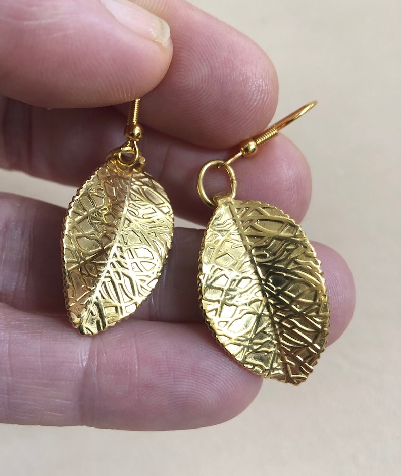 Puede incluir: Un par de pendientes de hoja de oro con una superficie texturizada. Los pendientes tienen un dise&ntilde;o simple y son perfectos para el uso diario.