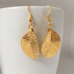 Puede incluir: Un par de pendientes de hoja de oro con un dise&ntilde;o delicado e intrincado. Los pendientes est&aacute;n hechos de metal y tienen un acabado brillante.