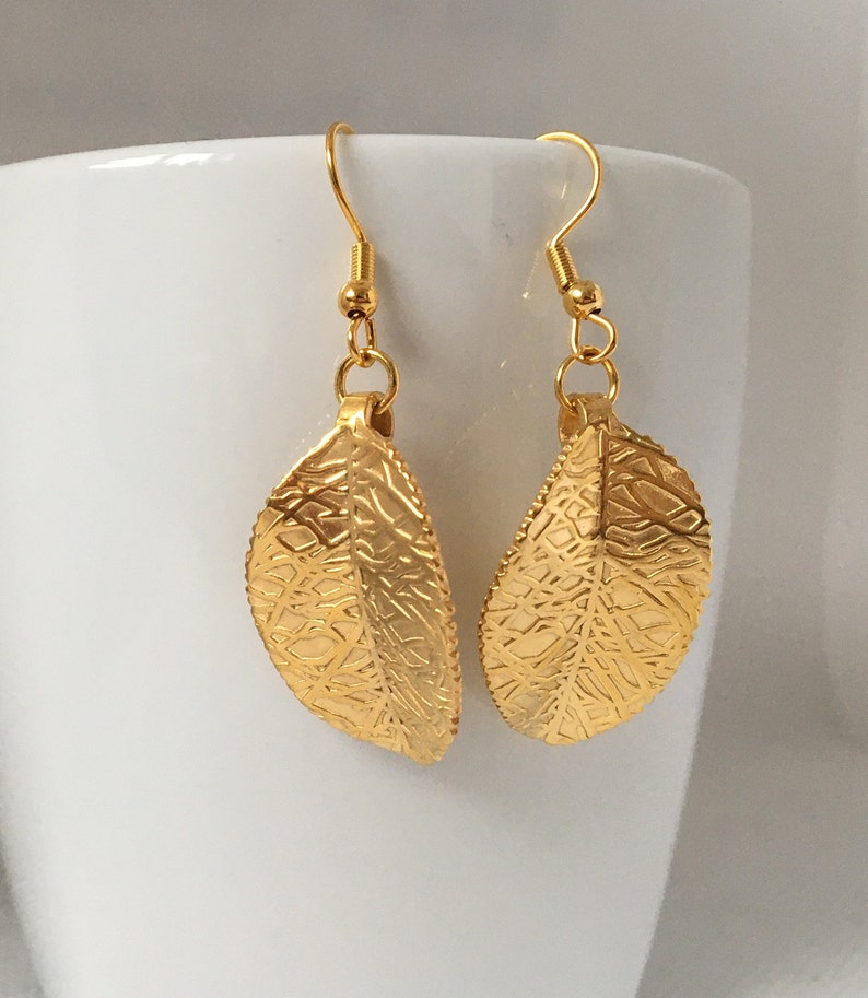 Puede incluir: Un par de pendientes de hoja de oro con un dise&ntilde;o delicado e intrincado. Los pendientes est&aacute;n hechos de metal y tienen un acabado brillante.