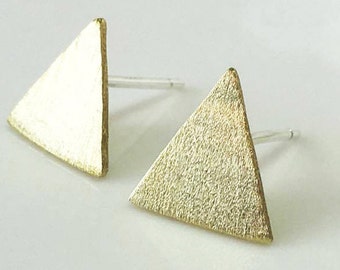 Puede incluir: Un par de pendientes de botón triangulares dorados. Los pendientes tienen una superficie texturizada y están sobre un fondo blanco. Los pendientes son pequeños y geométricos.