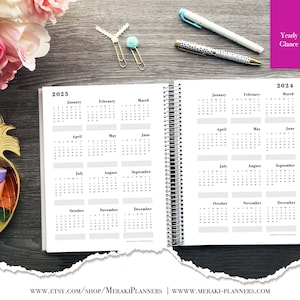 Puede incluir: Un planificador de espiral abierto que muestra calendarios anuales para 2023 y 2024. Las p&aacute;ginas son blancas con texto negro, mostrando meses y fechas. El planificador est&aacute; sobre una superficie de madera oscura, con bol&iacute;grafos y elementos decorativos.